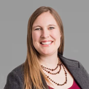 Anne Stoll, CPA, headshot. She has long straight brown hair and is wearing a grey blazer, maroon shirt and a beaded necklace.